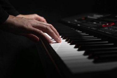 Uzun ince parmaklı bir çift el, yumuşak dramatik bir ışıkla aydınlanan dijital piyanonun beyaz tuşlarına yavaşça bastırır..