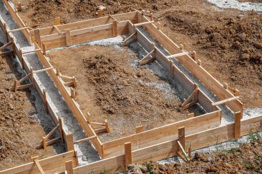 İnşaat alanındaki toprak ve çakıllarla çevrili ahşap bir yapı üzerine beton bir temel dökülüyor..