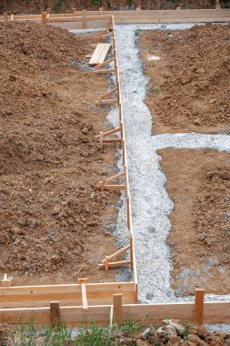 İnşaat alanındaki toprak ve çakıllarla çevrili ahşap bir yapı üzerine beton bir temel dökülüyor..