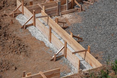 İnşaat alanındaki toprak ve çakıllarla çevrili ahşap bir yapı üzerine beton bir temel dökülüyor..