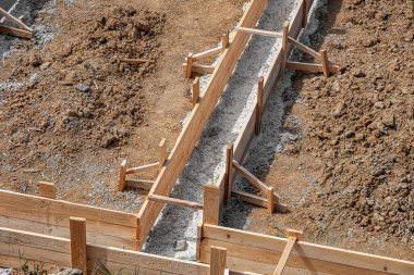 İnşaat alanındaki toprak ve çakıllarla çevrili ahşap bir yapı üzerine beton bir temel dökülüyor..