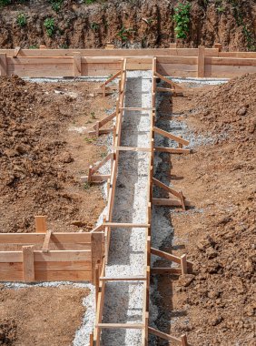 İnşaat alanındaki toprak ve çakıllarla çevrili ahşap bir yapı üzerine beton bir temel dökülüyor..