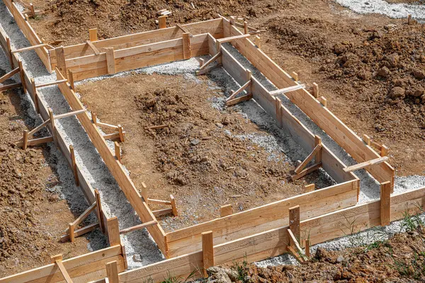 İnşaat alanındaki toprak ve çakıllarla çevrili ahşap bir yapı üzerine beton bir temel dökülüyor..