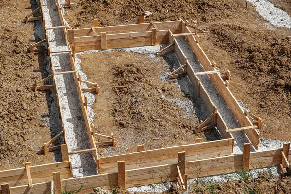 İnşaat alanındaki toprak ve çakıllarla çevrili ahşap bir yapı üzerine beton bir temel dökülüyor..