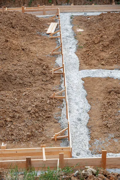 İnşaat alanındaki toprak ve çakıllarla çevrili ahşap bir yapı üzerine beton bir temel dökülüyor..