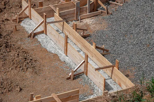 İnşaat alanındaki toprak ve çakıllarla çevrili ahşap bir yapı üzerine beton bir temel dökülüyor..