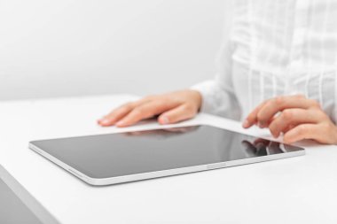 Beyaz gömlekli bir insan beyaz bir masada tabletle etkileşime geçer..