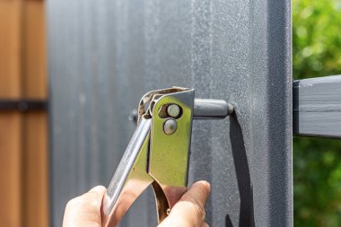 Perçin kullanan bir insan elleri, çit ya da yapı için siyah kıvrımlı metal bir levha takar..