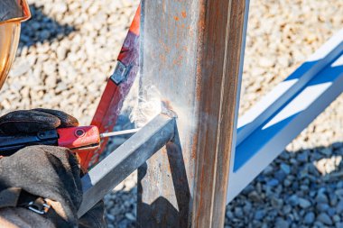 Görünür kıvılcımlar, duman ve koruyucu eldivenlerle birlikte iki metal kirişi birbirine kaynaştıran bir işçinin yakın çekim görüntüsü yüksek ısı üretim sürecini gösteriyor..