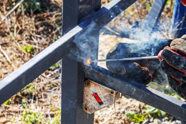 Görünür kıvılcımlar, duman ve koruyucu eldivenlerle birlikte iki metal kirişi birbirine kaynaştıran bir işçinin yakın çekim görüntüsü yüksek ısı üretim sürecini gösteriyor..
