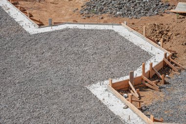 Yeni dökülmüş beton bir temel ve patika, ahşap biçimlendirme çerçeveli ve gevşek çakıl ve kahverengi toprak ile çevrili güneşli bir inşaat alanında.