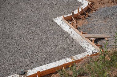 Yeni dökülmüş beton bir temel ve patika, ahşap biçimlendirme çerçeveli ve gevşek çakıl ve kahverengi toprak ile çevrili güneşli bir inşaat alanında.