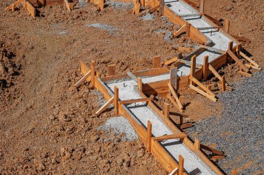 Taze betonla dolu ahşap işlemeli bir bina inşaatın erken safhalarında bir inşaat sahasında gösteriliyor.