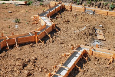 Taze betonla dolu ahşap işlemeli bir bina inşaatın erken safhalarında bir inşaat sahasında gösteriliyor.