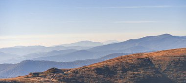 Yumuşak ışıkta yıkanan katmanlı dağ sırtlarının panoramik görüntüsü sakin ve sakin bir doğal manzara yaratıyor..