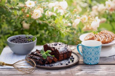 tatlı hamur işleri, kruvasanlar, çikolatalı kekler, yabanmersini, çay ve kahve ağaçtan bir masada çiçek açan bahçede.