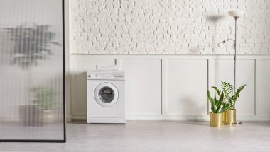 Washing machine in the bathroom, white brick wall background, vase of plant, cabinet and marble floor, folding screen.