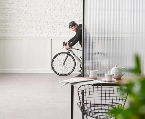 Man with bike in the room, chair table desk white brick and classic wall, blur green leaf.