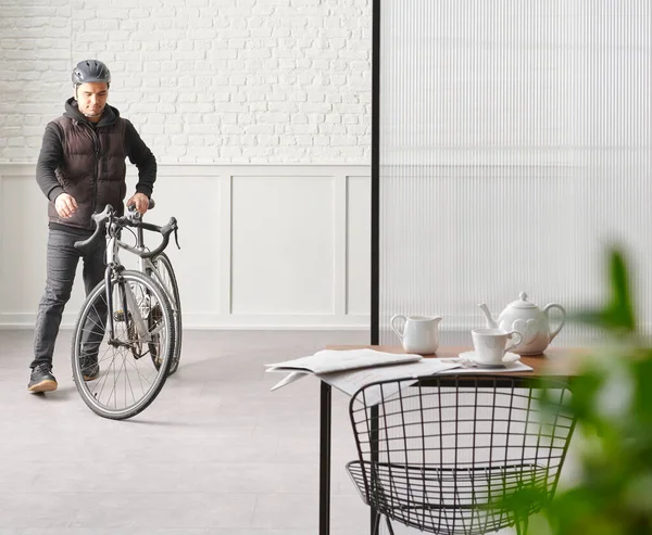 Man with bike in the room, chair table desk white brick and classic wall, blur green leaf.