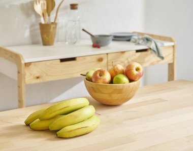 Tahta masadaki meyve sepetini, mutfak arka planını, muzu, elmayı ve armudu kapat..