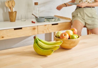 Ahşap masanın, mutfağın, muzun, elmanın ve armutun üzerindeki meyve sepetini kapat. Kadın arkaplan biçimi.