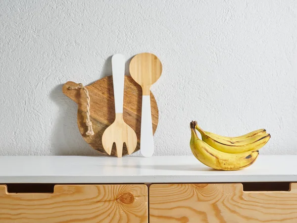 Yellow banana kitchen style, wooden table, water cutting board. Wood fork and spoon.