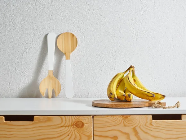 Yellow banana kitchen style, wooden table, water cutting board. Wood fork and spoon.