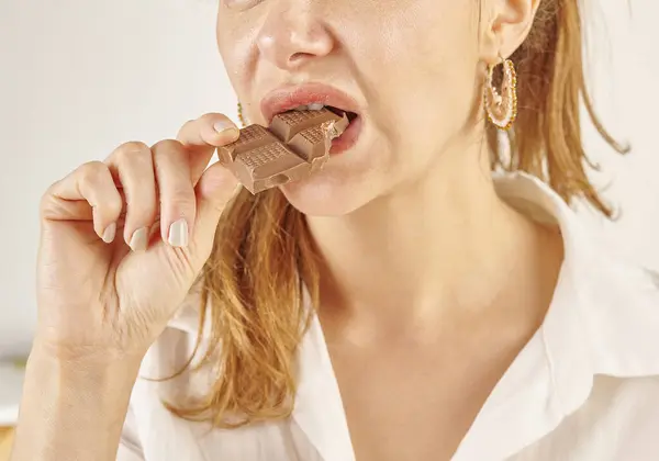 Woman eating chocolate, close-up, mouth and hand. Kitchen background style.