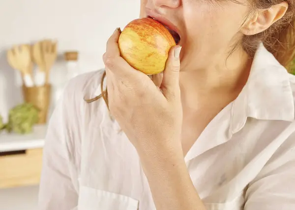 Woman eating apple, close-up, mouth and hand. Kitchen background style.