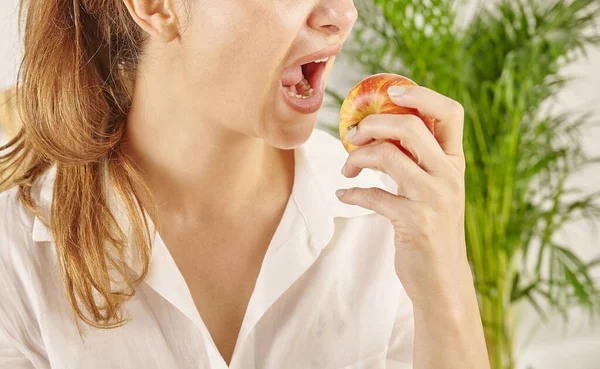 Woman eating apple, close-up, mouth and hand. Kitchen background style.