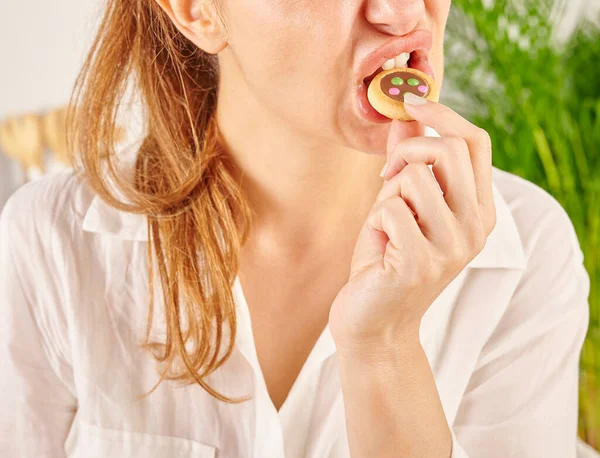 Woman eating biscuit, close-up, mouth and hand. Kitchen background style.