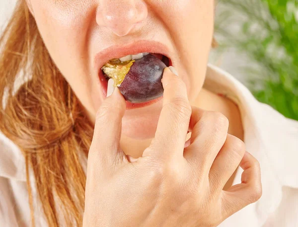 Woman eating plum, close-up, mouth and hand. Kitchen background style.