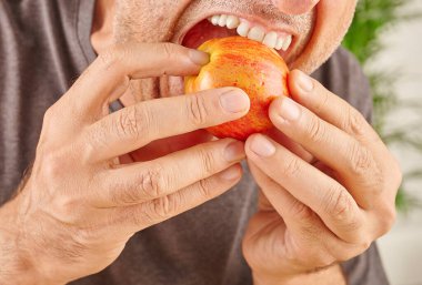 Kırmızı elma yiyen adamın ağzını kapat. Mutfak arka planı.