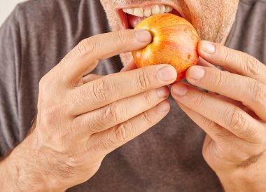 Kırmızı elma yiyen adamın ağzını kapat. Mutfak arka planı.