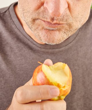 Kırmızı elma yiyen adamın ağzını kapat. Mutfak arka planı.