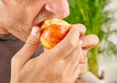 Kırmızı elma yiyen adamın ağzını kapat. Mutfak arka planı.