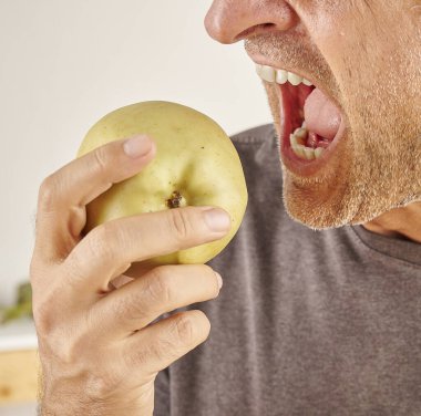 Kırmızı elma yiyen adamın ağzını kapat. Mutfak arka planı.