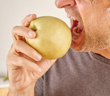 Kırmızı elma yiyen adamın ağzını kapat. Mutfak arka planı.