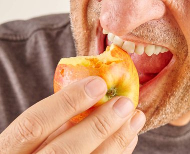 Elma yiyen adam, yakın plan, el ve ağız. Mutfak arka planı.