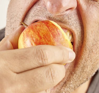 Elma yiyen adam, yakın plan, el ve ağız. Mutfak arka planı.