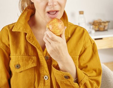 Kadın elma yiyor, yakın plan, el ve ağız. Mutfak arka planı.