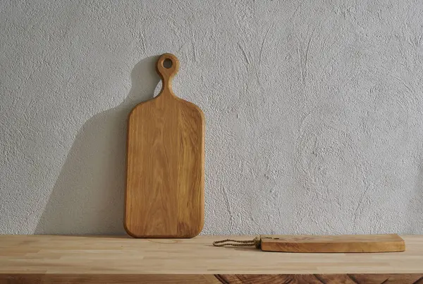 Wooden cutting board on the table, kitchenware, vase of plant grey decorative wall background.