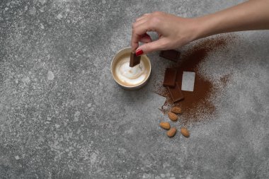 Seramik cam kahve stili, arka planda çikolata ve badem, gri dekoratif tasarım. Kadın eli.