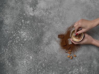 Seramik cam kahve stili, arka planda çikolata ve badem, gri dekoratif tasarım. Kadın eli.