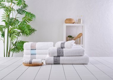 Arka arkaya beyaz ve gri havlular, banyo odası eşyalarıyla dolu vazo..