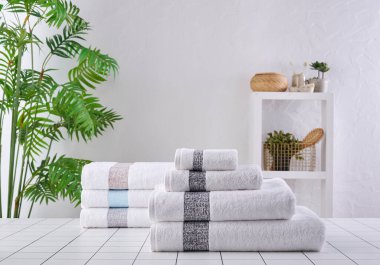 Arka arkaya beyaz ve gri havlular, banyo odası eşyalarıyla dolu vazo..