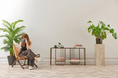 Bir kadın evde kitap okuyor, telefon ve tablete bakıyor. Bitkinin dekoratif iç stili ve vazosu.