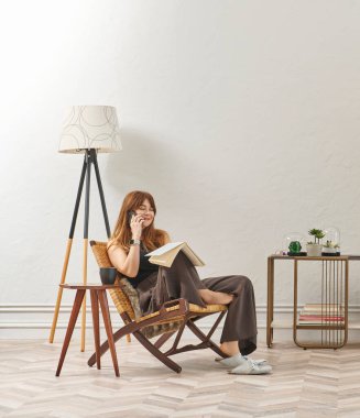 Bir kadın evde kitap okuyor, telefon ve tablete bakıyor. Bitkinin dekoratif iç stili ve vazosu.