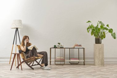 Bir kadın evde kitap okuyor, telefon ve tablete bakıyor. Bitkinin dekoratif iç stili ve vazosu.