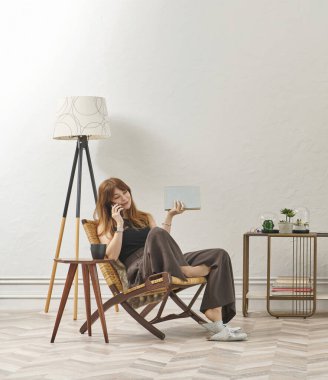 Bir kadın evde kitap okuyor, telefon ve tablete bakıyor. Bitkinin dekoratif iç stili ve vazosu.